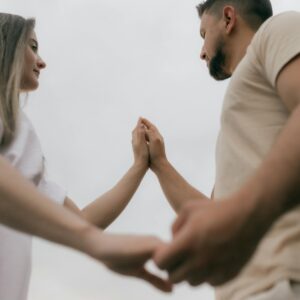 A couple connecting and holding hands against a cloudy sky, symbolizing love and unity.