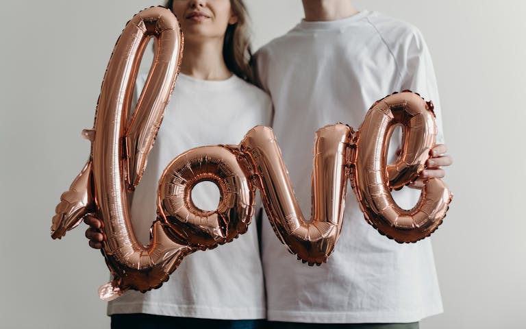 A couple in blank white t-shirts holding a metallic 'love' balloon emphasizing romance and joy.