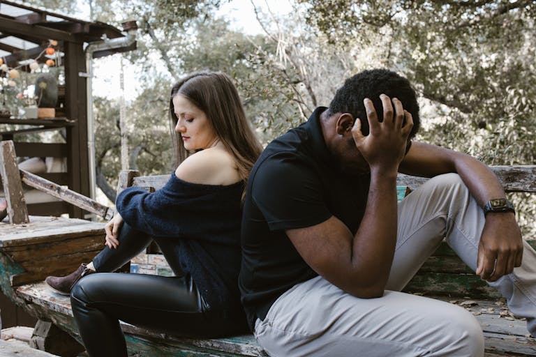 A couple sits back to back on a bench, depicting emotional conflict and loneliness.