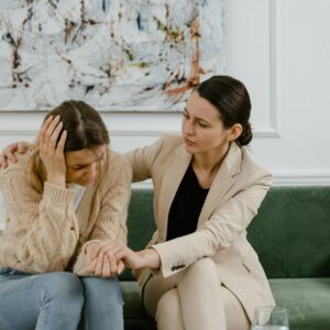 A woman comforts a friend in distress on a green couch indoors.