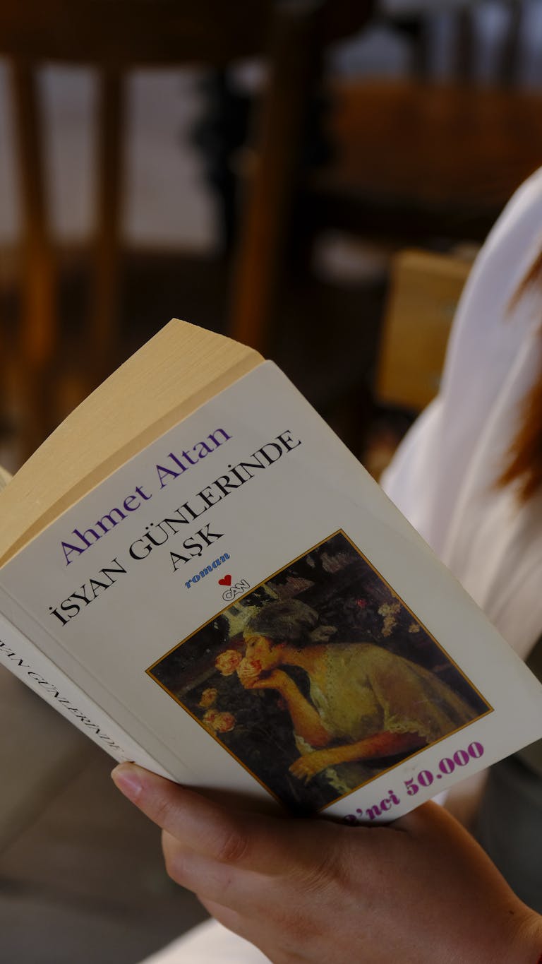 Close-up shot of a woman holding and reading a Turkish novel by Ahmet Altan.