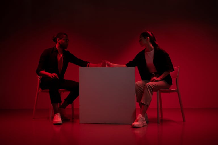 Dramatic studio capture of a couple in red lighting, seated at a table in stylish attire.