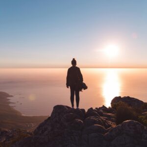 Silhouette of a person standing on a rocky cliff, enjoying the stunning sunset over the ocean in Cape Town.