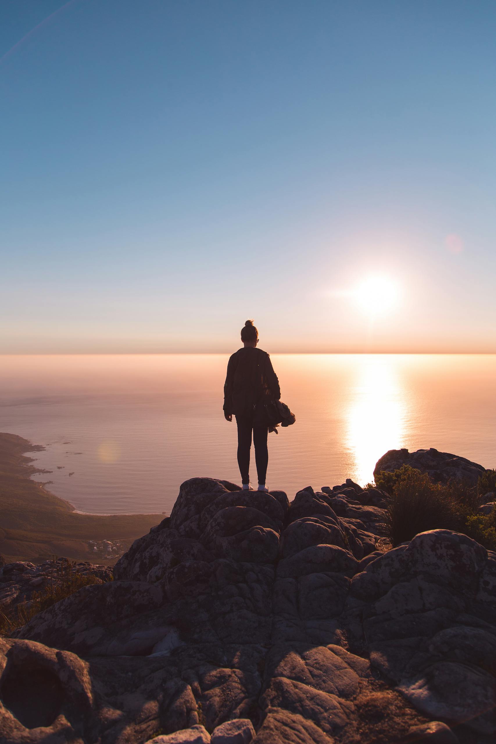 Silhouette of a person standing on a rocky cliff, enjoying the stunning sunset over the ocean in Cape Town.